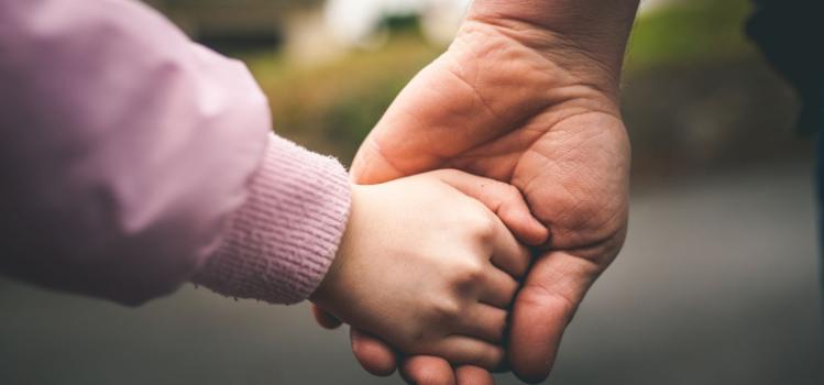 Image of adult and child holding hands against a background of asphalt and bushes